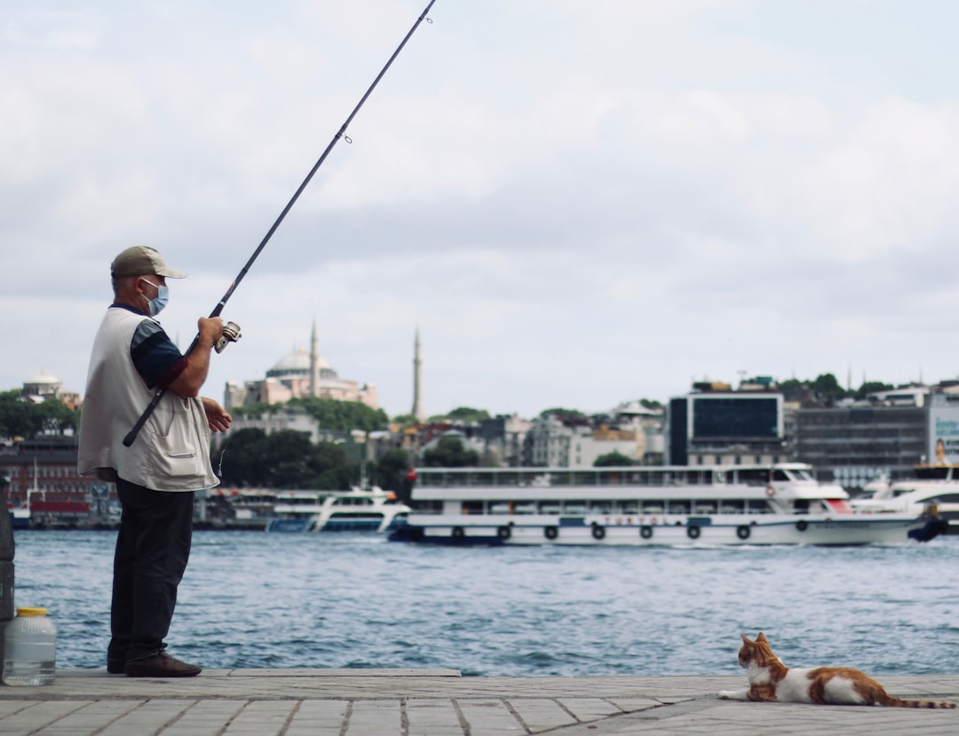 man in white t-shirt and blue denim jeans holding fishing rod