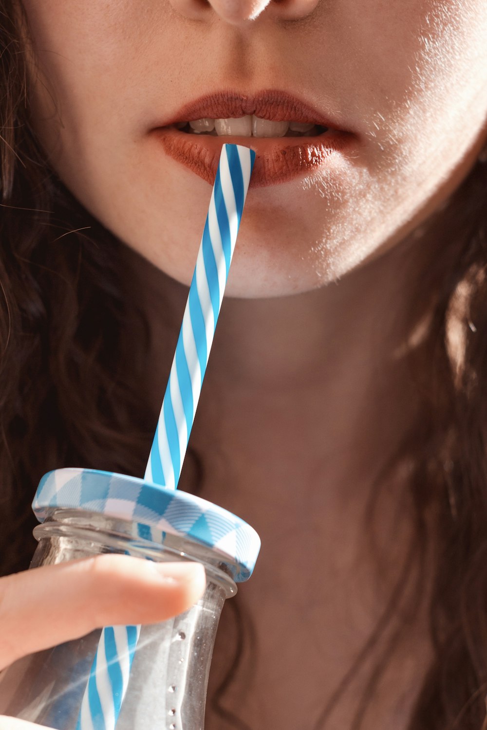 woman sipping on clear glass jar with pink and blue straw