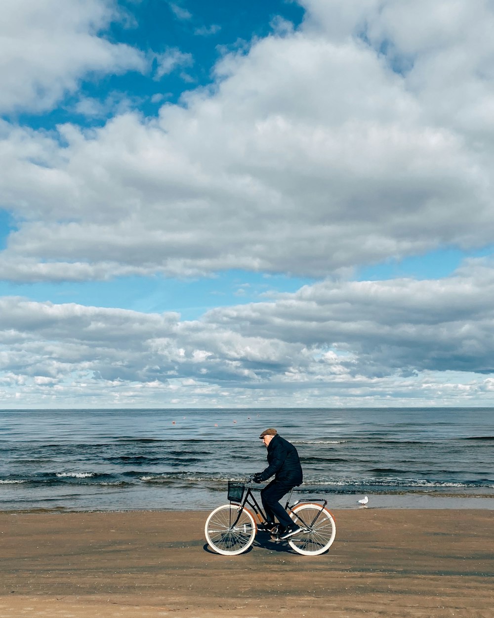 낮 동안 해변에서 자전거를 타는 검은 재킷을 입은 남자