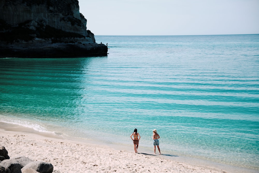 2 women in bikini standing on beach during daytime