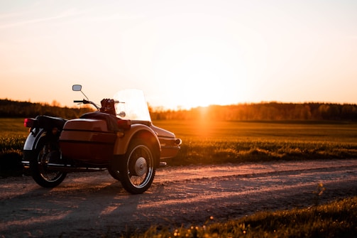 A vintage motorcycle parked beside a rustic road under a warm sunset.