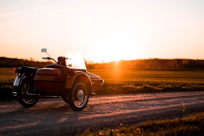 A vintage racing car and a motocross bike side by side on a dirt track at sunset.