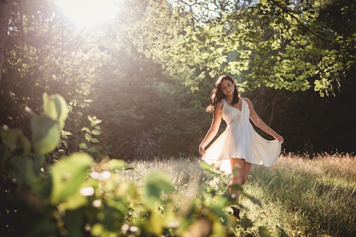 A serene scene of a model draped in flowing fabrics, standing in a sunlit forest clearing.