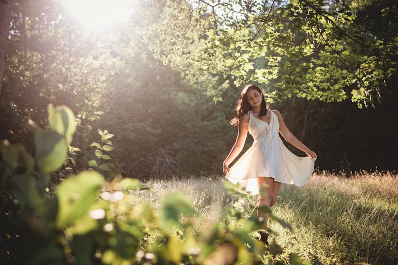 A serene model wearing a flowing, earth-toned dress standing in a sunlit forest clearing.