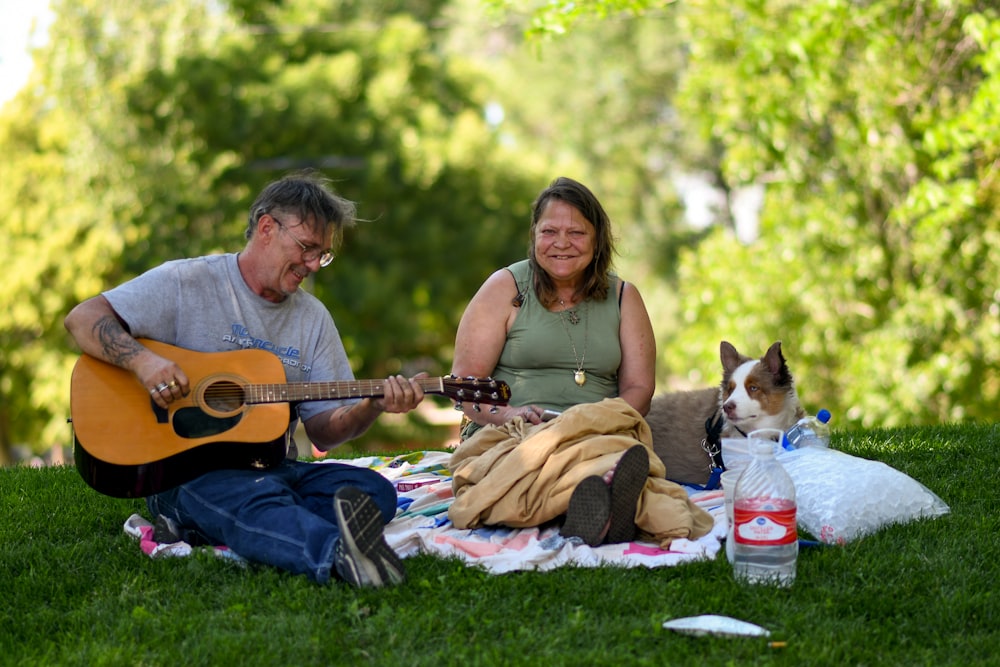 man and woman sitting on green grass field playing guitar during daytime
