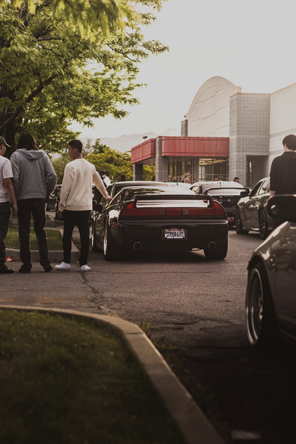 man in white t-shirt and black pants standing beside black car during daytime