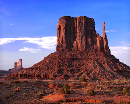 A sunlit desert mesa with rugged cliffs and sparse vegetation under a bright blue sky.