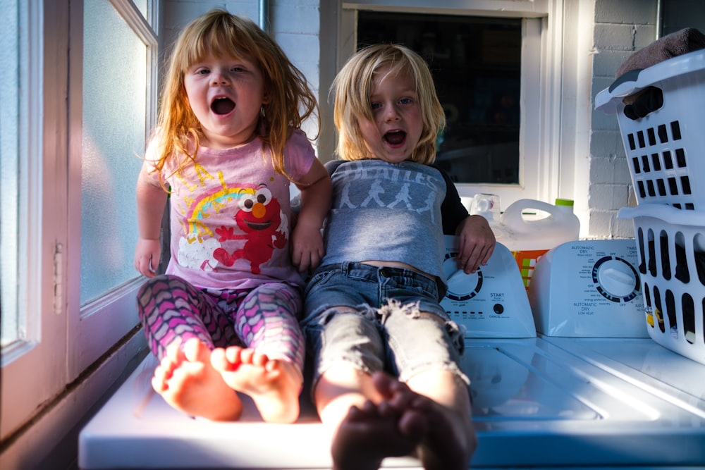 girl in pink and white crew neck t-shirt sitting beside girl in blue t-shirt