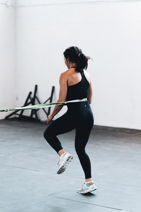 Woman in a fitted black racerback tank and leggings pulling a resistance band