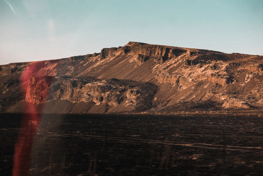 brown mountain beside body of water during daytime