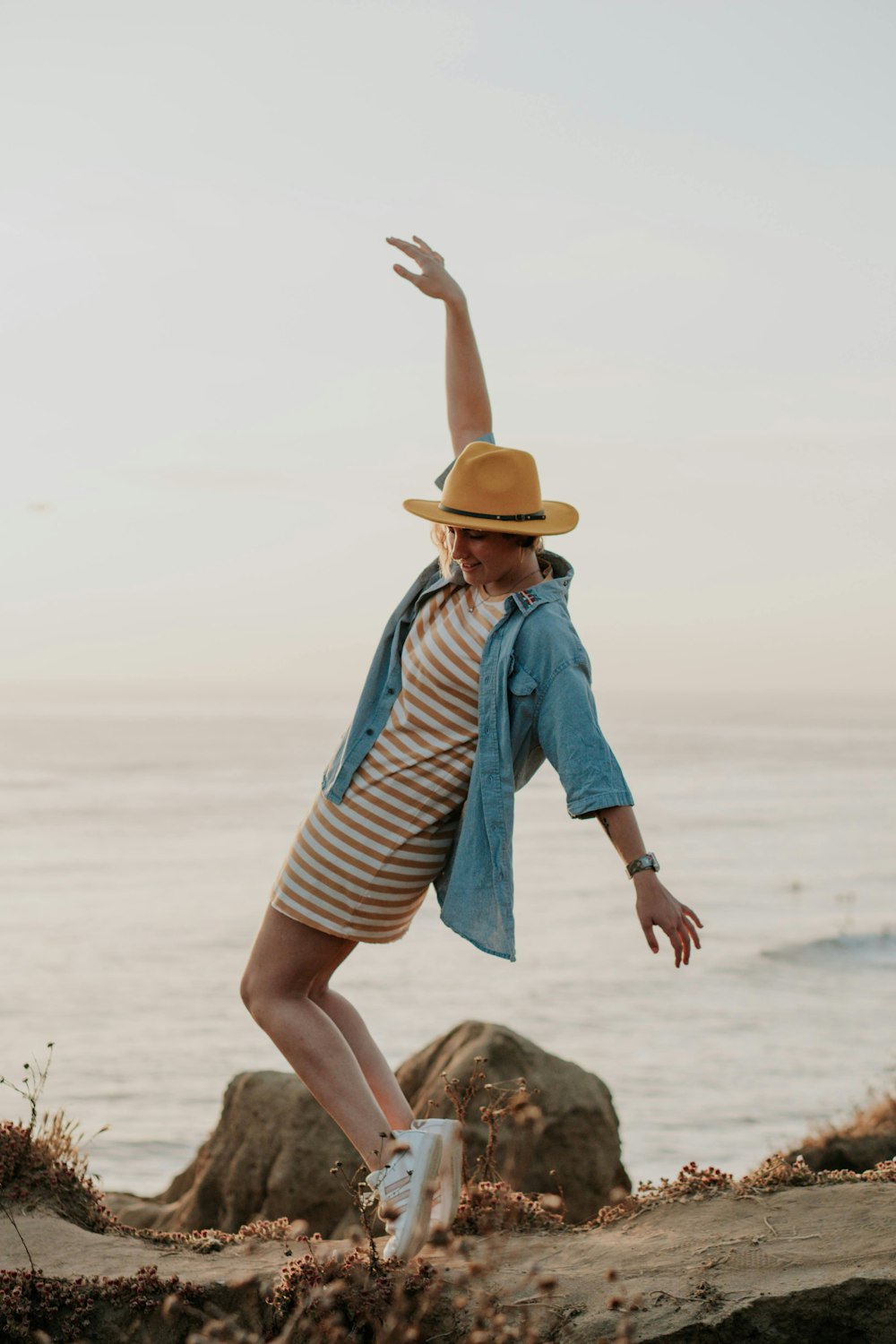 woman in blue and white striped shirt and brown hat sitting on sand during daytime