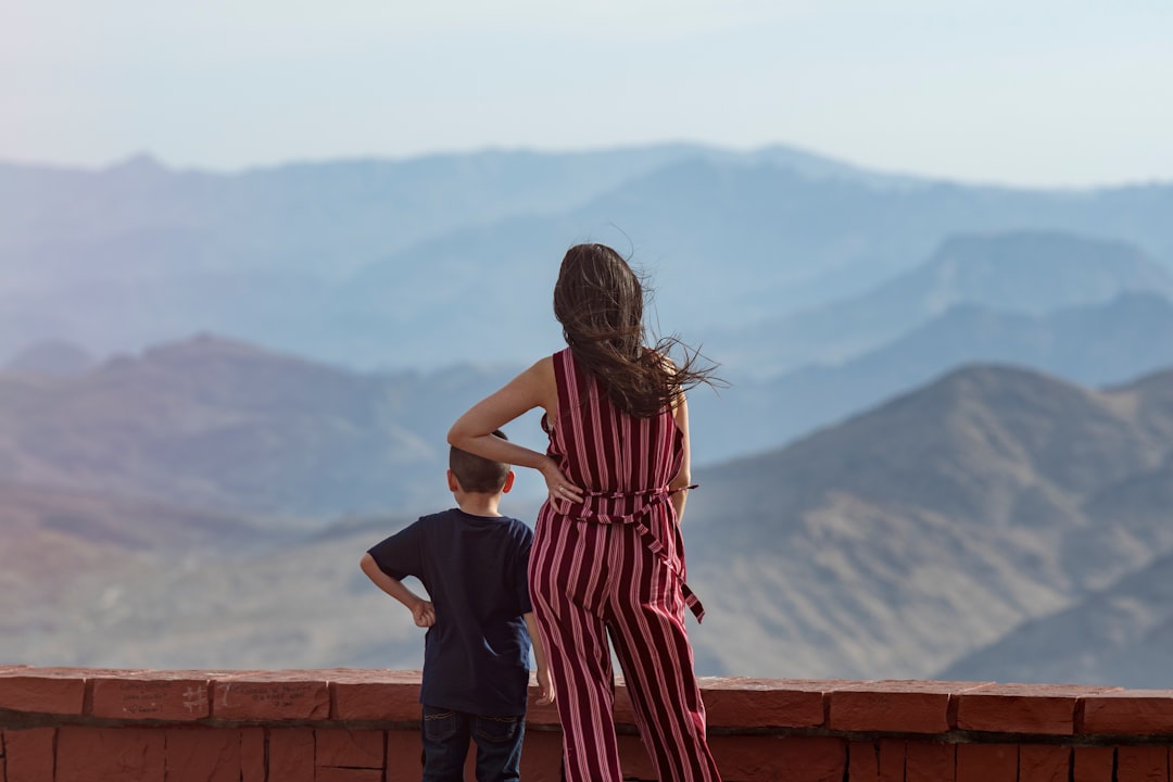 woman in black and red stripe dress standing on brown wooden fence during daytime