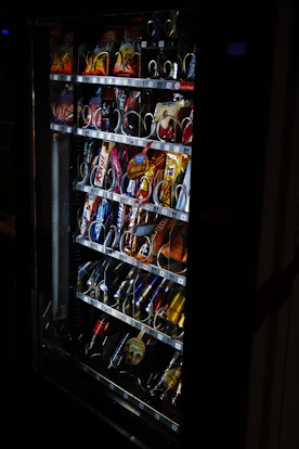 A sleek vending machine filled with assorted snacks and beverages, brightly lit in a modern setting.