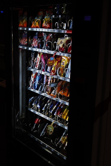 A sleek vending machine stocked with a variety of modern snacks and drinks, set against a bright office lobby.