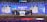 A group of people dressed in formal attire stands on a stage with a Nasdaq podium in the center. The backdrop displays the word 'BLUECITY' along with various smaller images of individuals. Confetti is falling, creating a celebratory atmosphere.