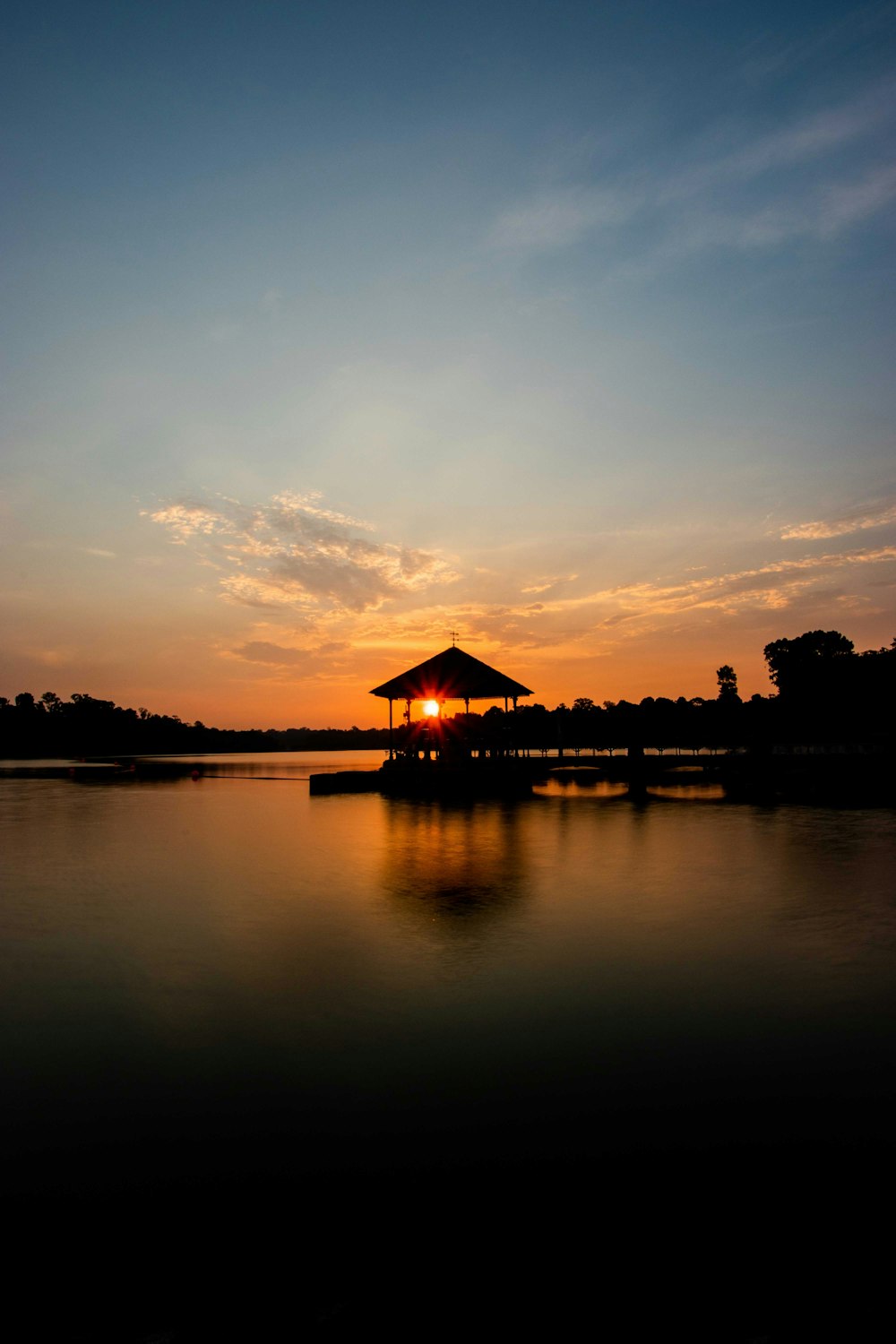 silhouette of house near body of water during sunset