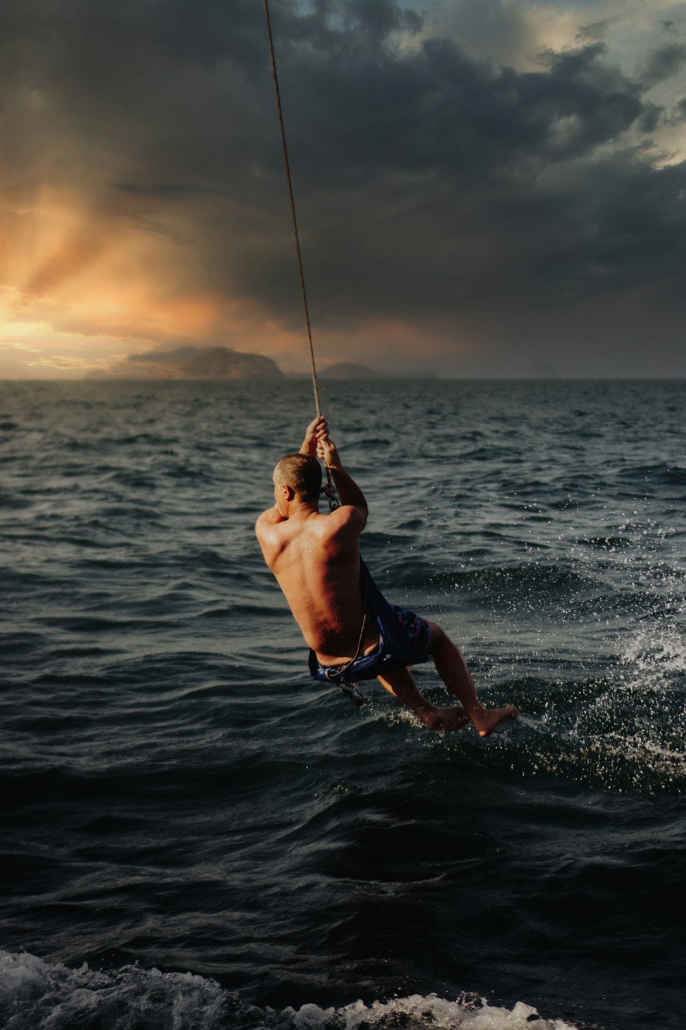 man in black shorts holding rope on body of water during daytime