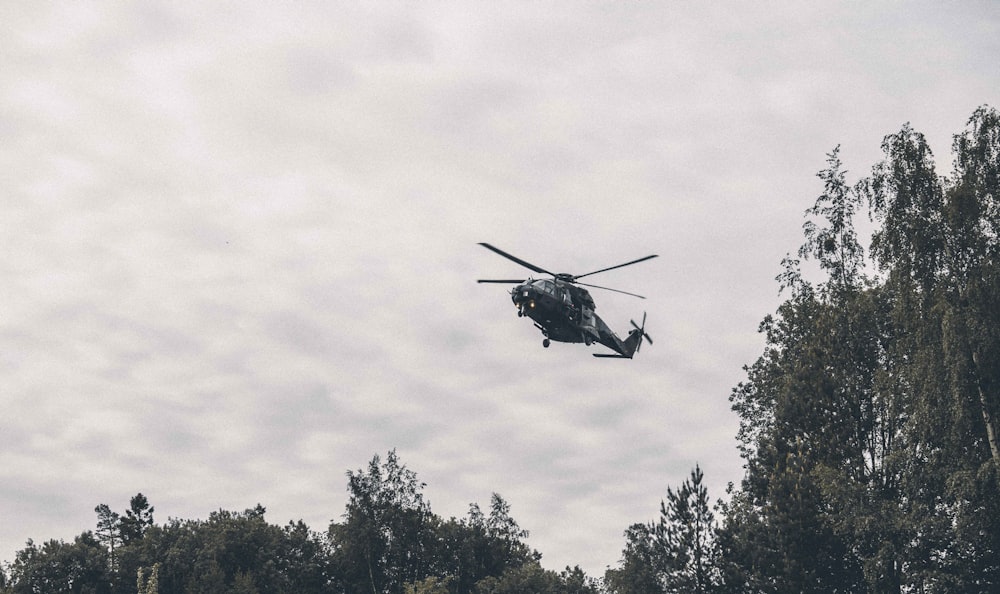 black helicopter flying over green trees during daytime