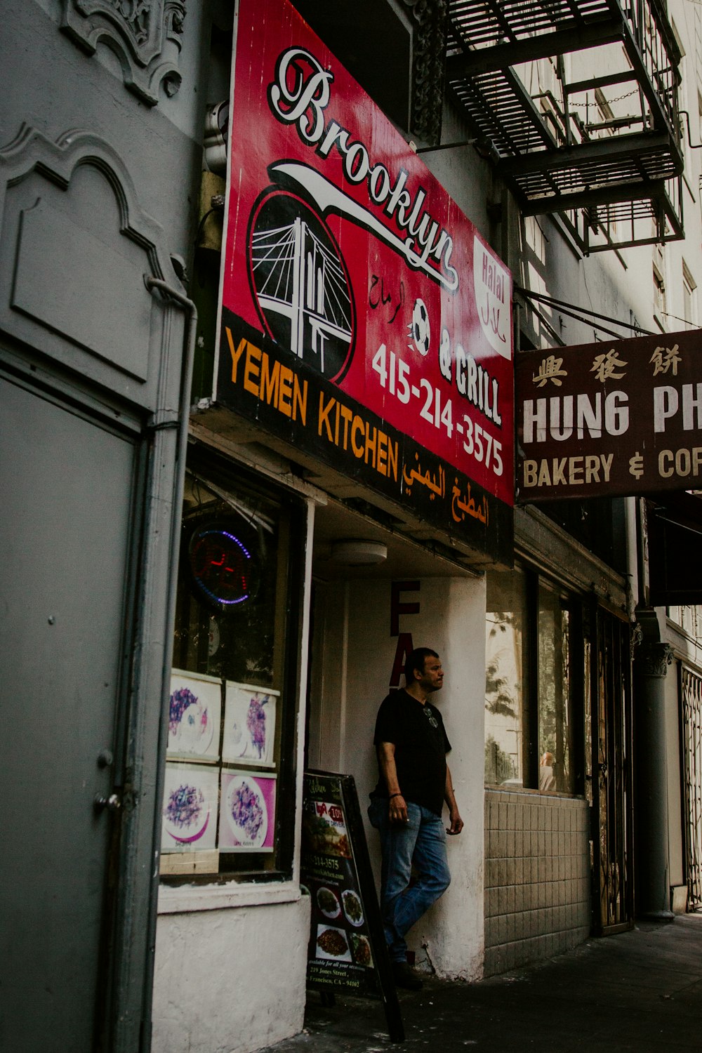 man in black t-shirt and blue denim jeans standing beside store during daytime