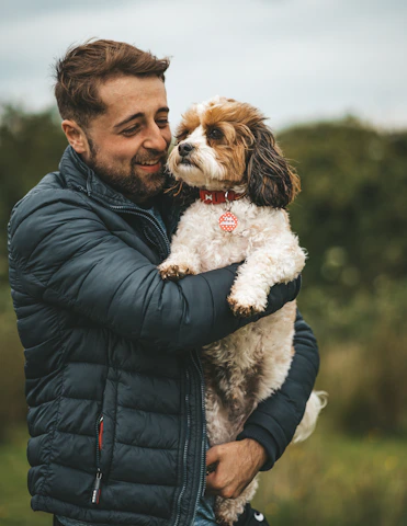 man in black leather jacket holding white and brown long coated small dog