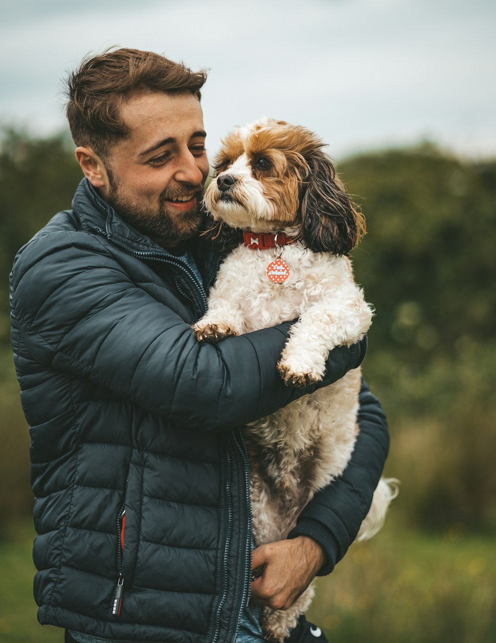 man in black leather jacket holding white and brown long coated small dog