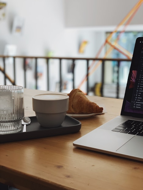 A cozy workspace with a laptop, coffee cup, and shopping bags on a wooden table.