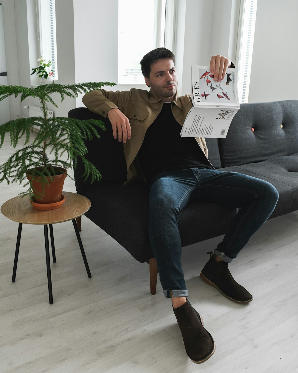 man in black polo shirt and blue denim jeans sitting on gray sofa