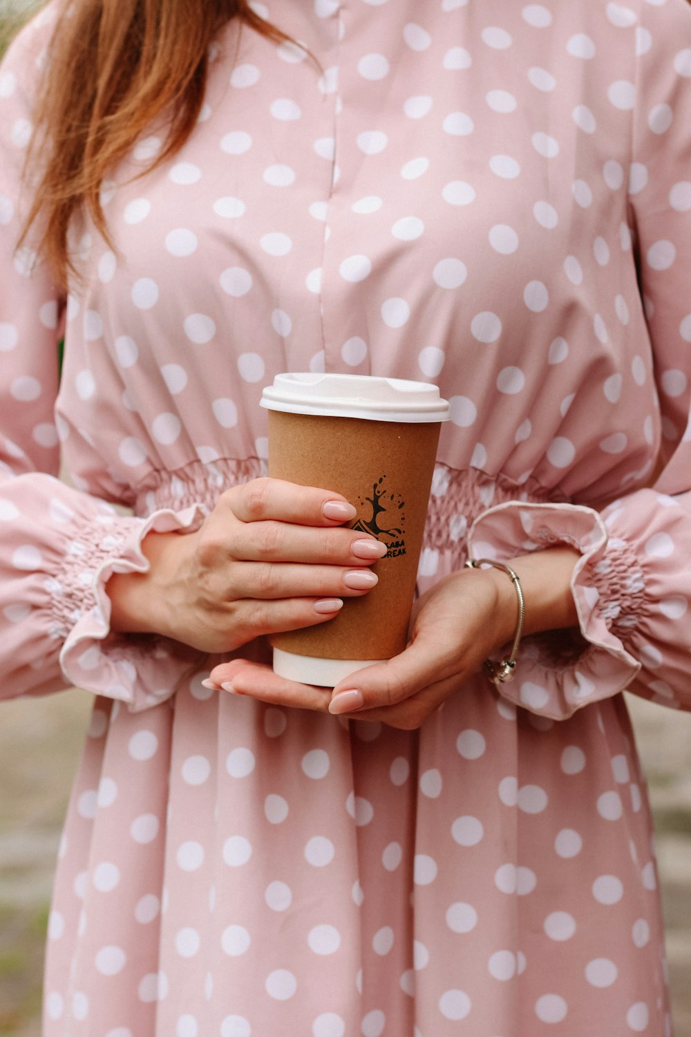 woman in pink and white polka dot robe holding brown cup