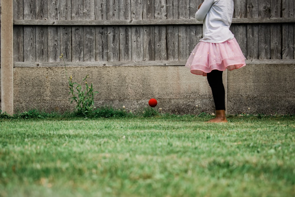 분홍색 치마와 흰색 긴팔 셔츠를 입은 소녀는 낮 동안 푸른 잔디밭에 서 있다