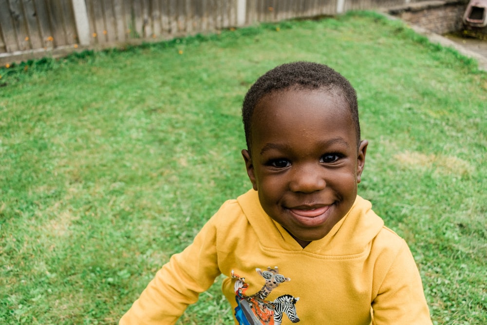 boy in yellow hoodie standing on green grass field during daytime