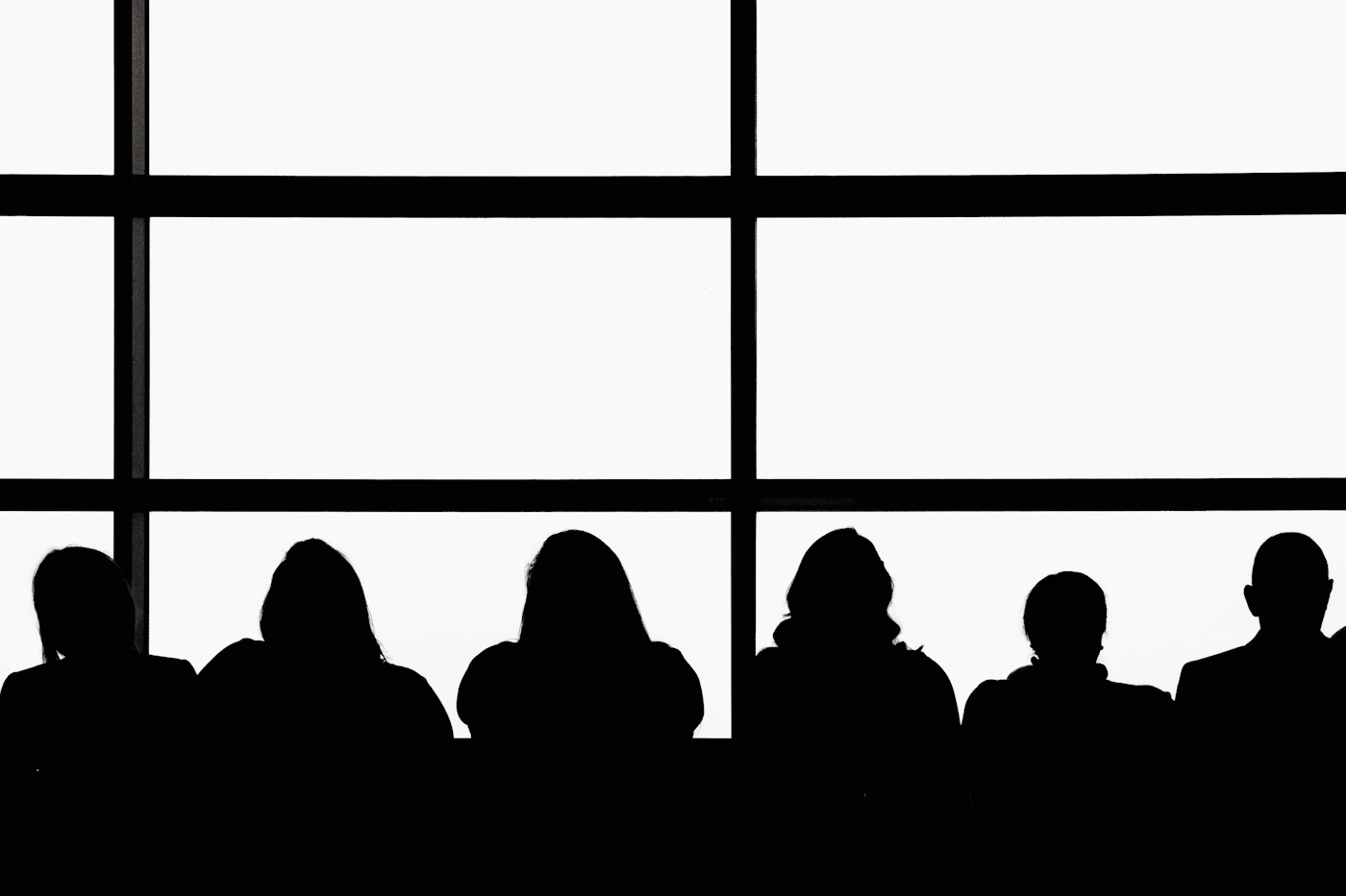 Silhouettes of a deal team seated in front of tall windows