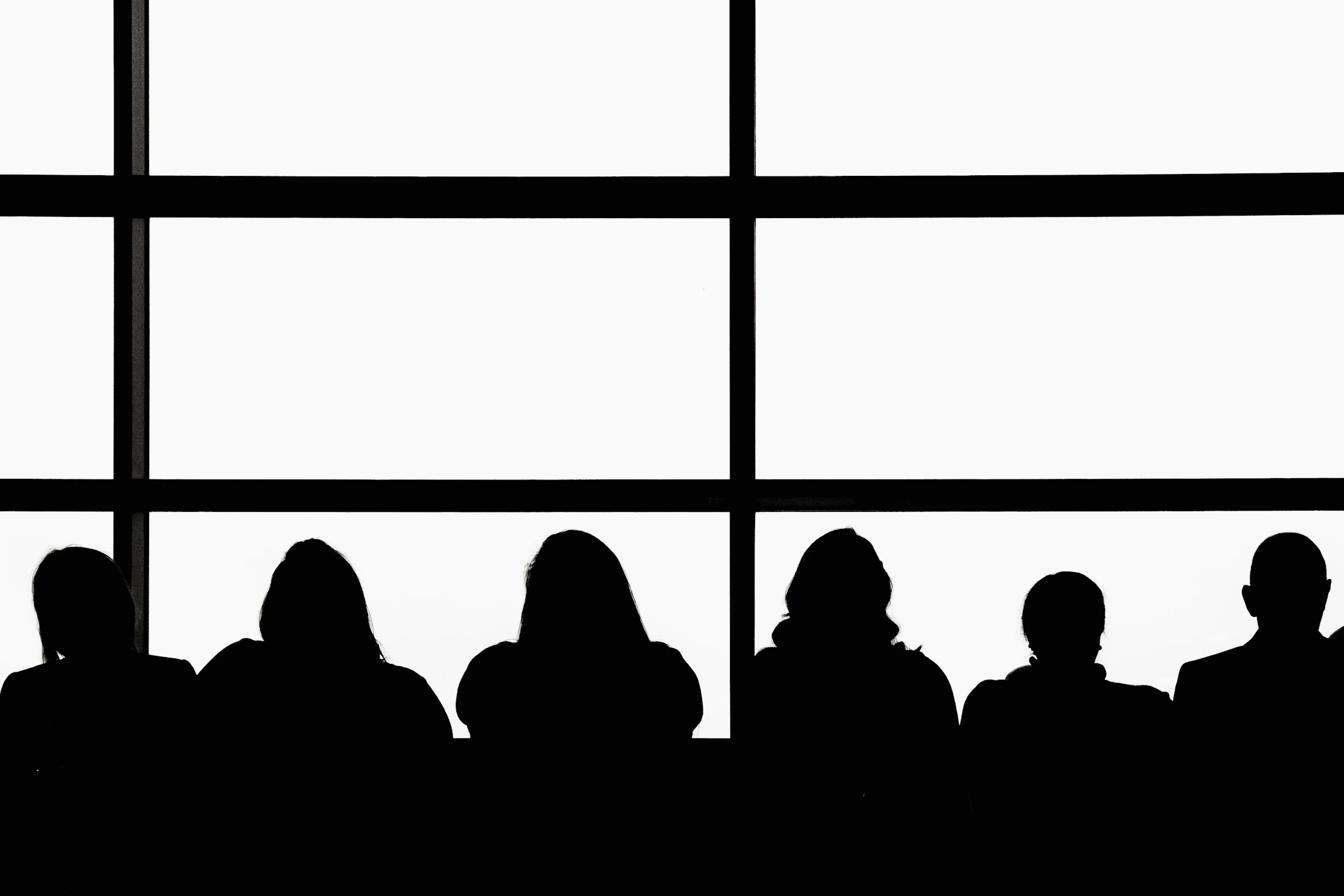 Silhouettes of a deal team seated in front of tall windows