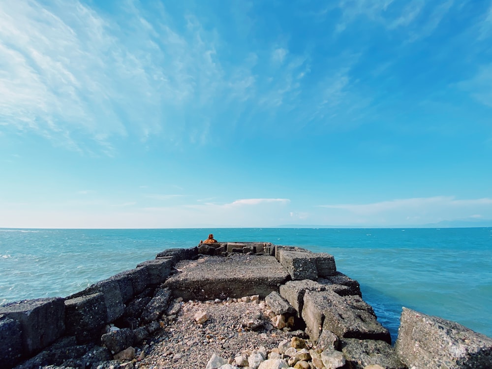 person sitting on rock formation near sea under blue sky during daytime