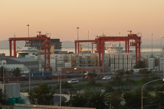 Photo of a large semi-truck parked at a busy shipping port during sunset.