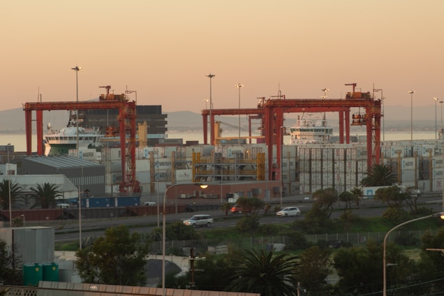 A cargo ship loaded with containers at a busy port during sunset.