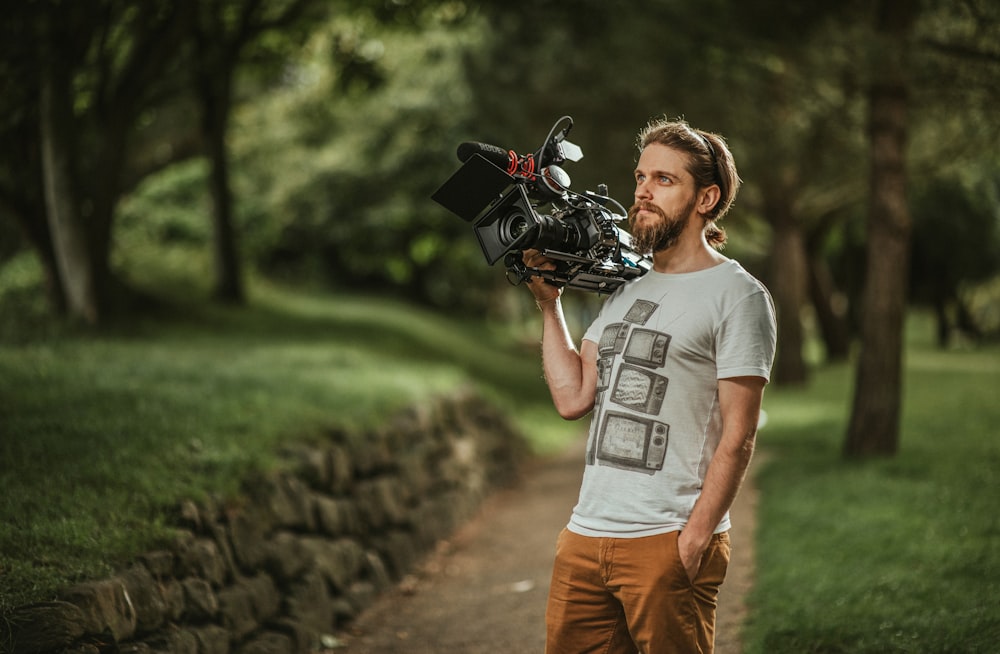 homem em camiseta cinza pescoço da tripulação e calças marrons segurando câmera dslr preta