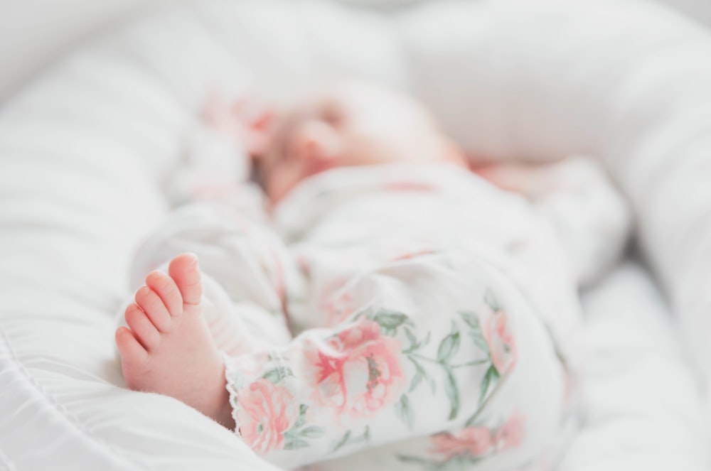 흰색과 빨간색 꽃무늬 옷을 입은 아기가 침대에 누워 있습니다.