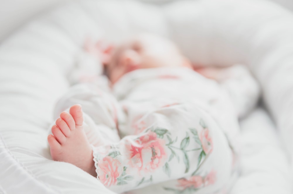 baby in white and red floral onesie lying on bed