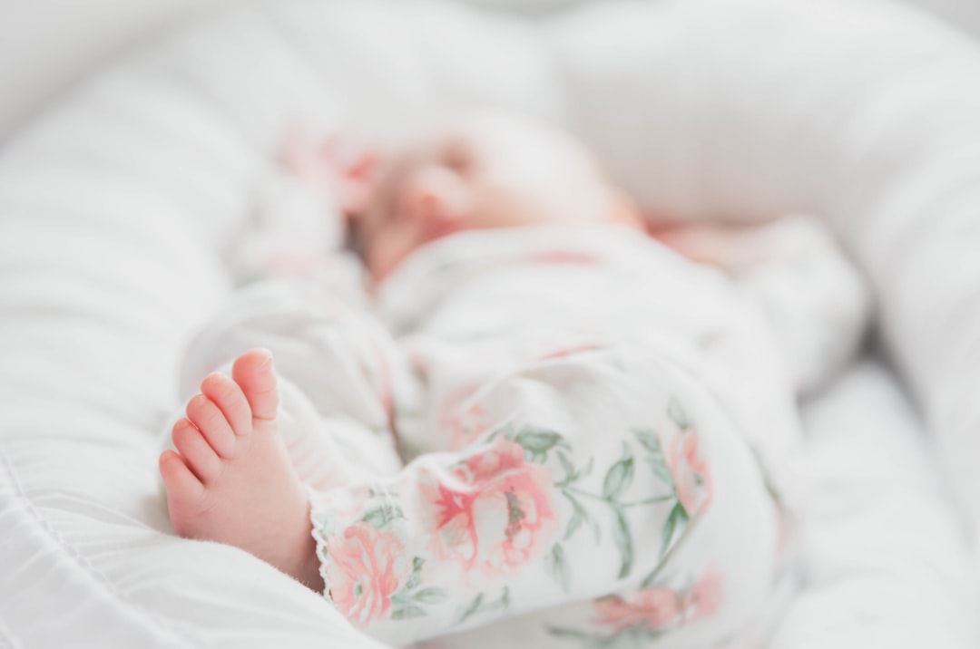 baby in white and red floral onesie lying on bed,