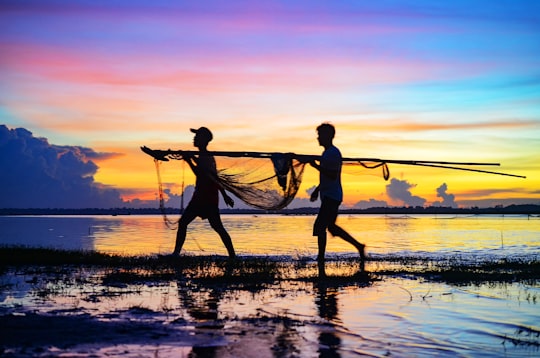 silhouette of 2 men holding fishing net on beach during sunset in Prey Veng Cambodia