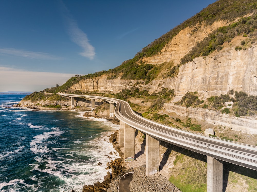 Ponte in cemento grigio sulla montagna rocciosa marrone accanto al mare blu sotto il cielo blu durante il giorno