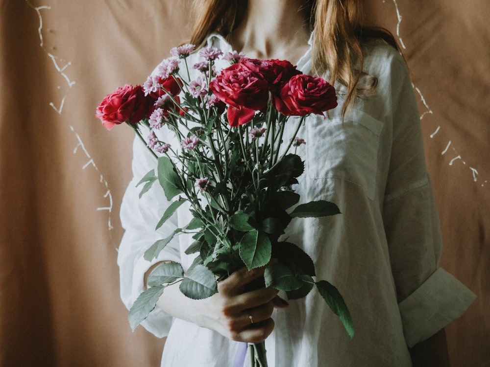 woman in white long sleeve shirt holding red rose