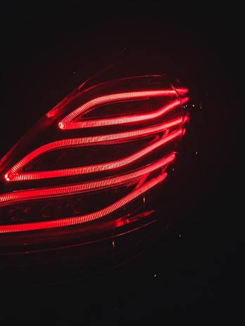 Red LED lights in a sleek, overlapping pattern create a modern appearance. The lights form part of a car's tail light, providing bright illumination against a dark background.