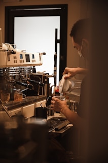 A barista carefully preparing a cup of tea with steam rising from the kettle.