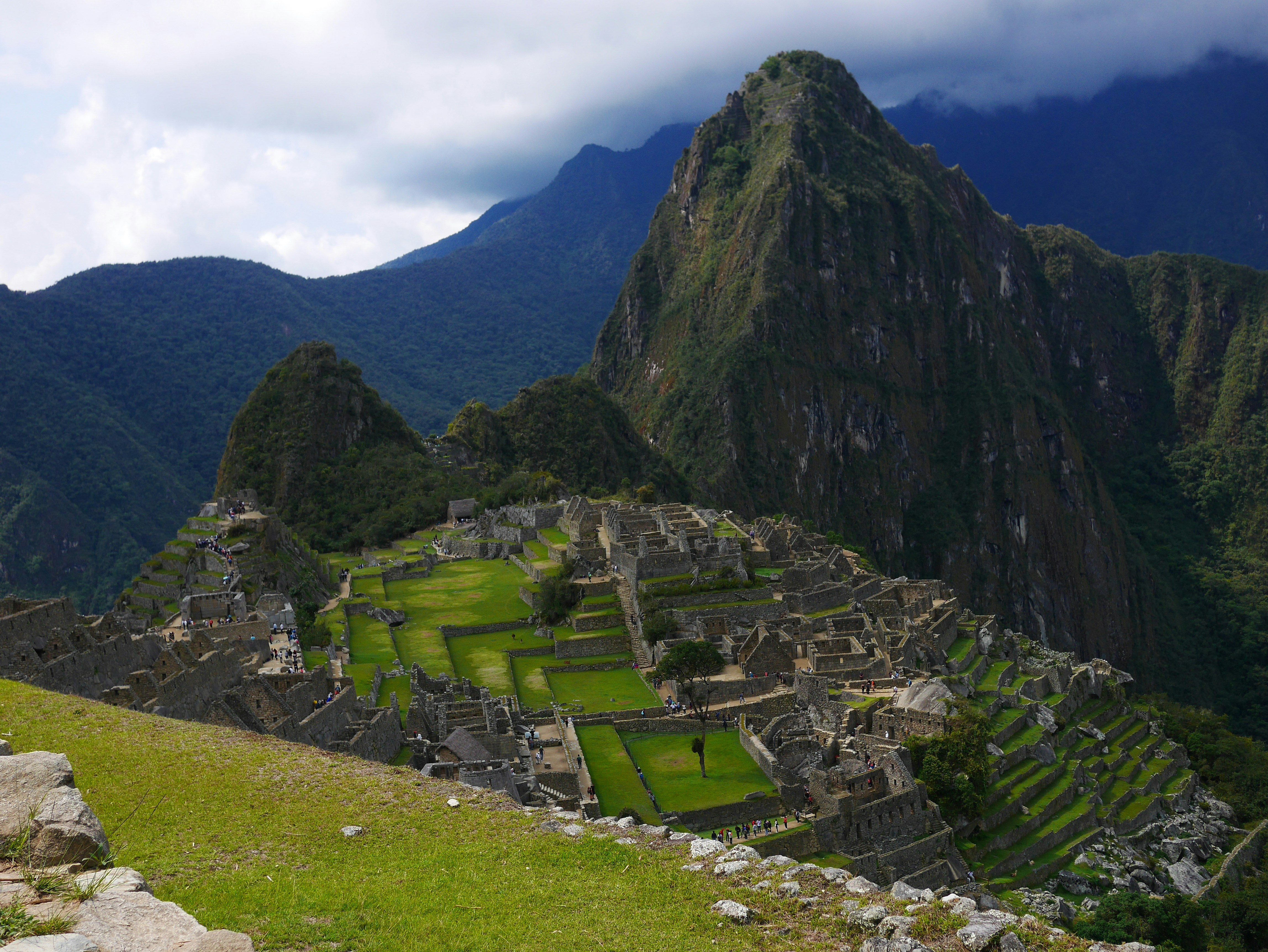 green grass field near mountain under white clouds during daytime