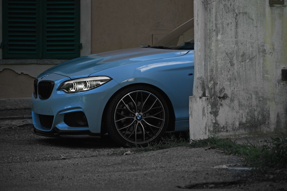 blue car parked beside gray concrete wall