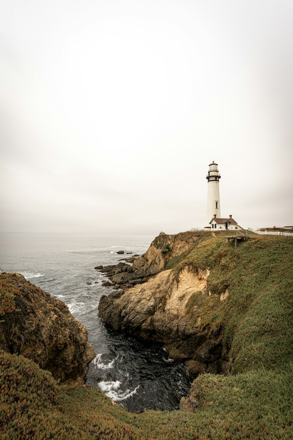 white lighthouse on brown rock formation near body of water during daytime