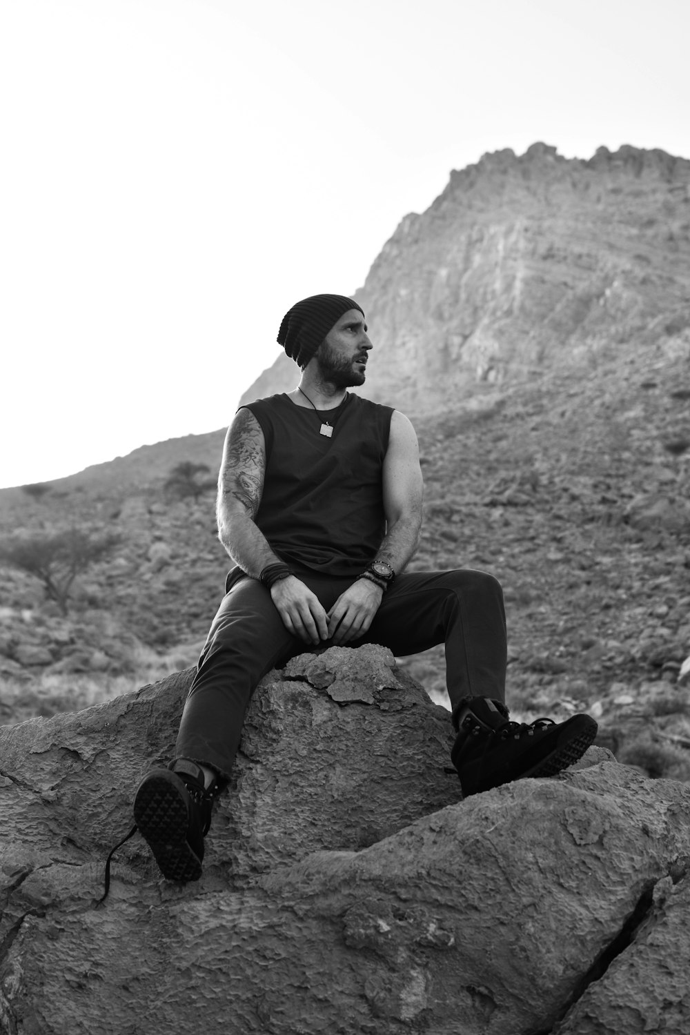 man in white tank top sitting on rock