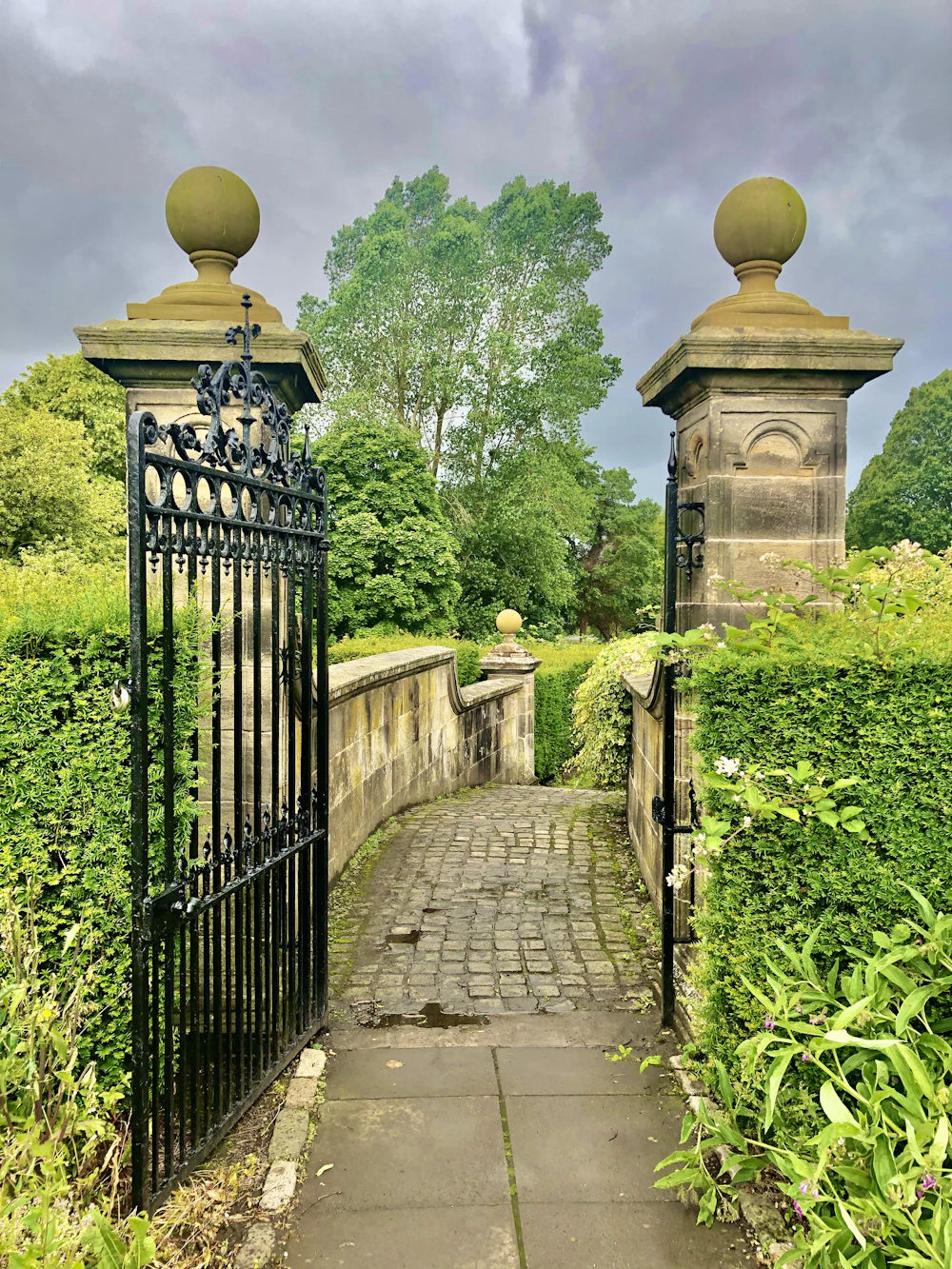 Heavy black wrought iron driveway gate with carved stone pillars at a hillside estate entrance