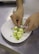 A pair of hands delicately arranging rolled zucchini appetizers filled with creamy cheese on a white oval plate. The dish features small dollops of dark sauce and green herb garnish on a stainless steel surface.